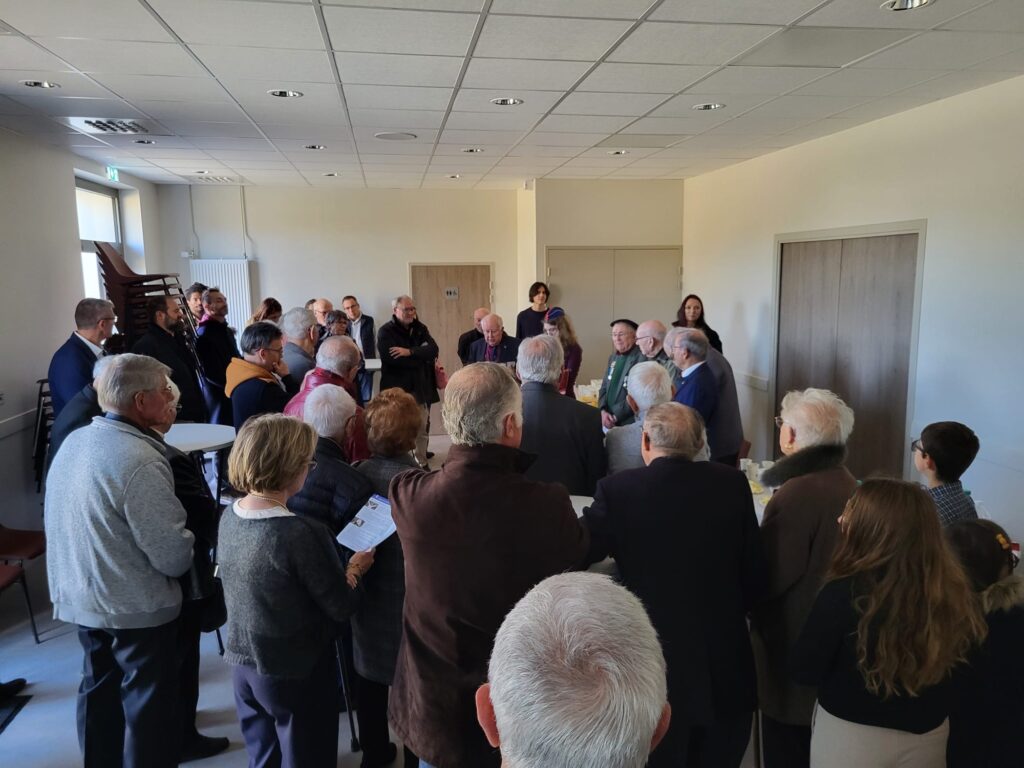 L'image montre un groupe de personnes rassemblées dans une salle, probablement pour une réunion ou un événement.