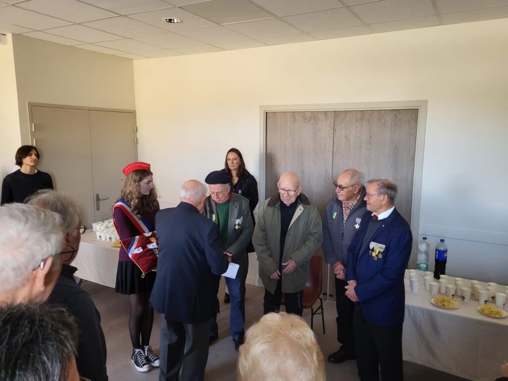 Un groupe de personnes, incluant des vétérans décorés, se rassemble dans une salle pour une cérémonie ou une réunion. 
