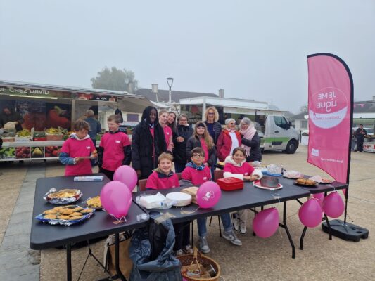 Un groupe de personnes, dont des enfants, posent devant une table avec des ballons roses et de la nourriture. Un stand de mar