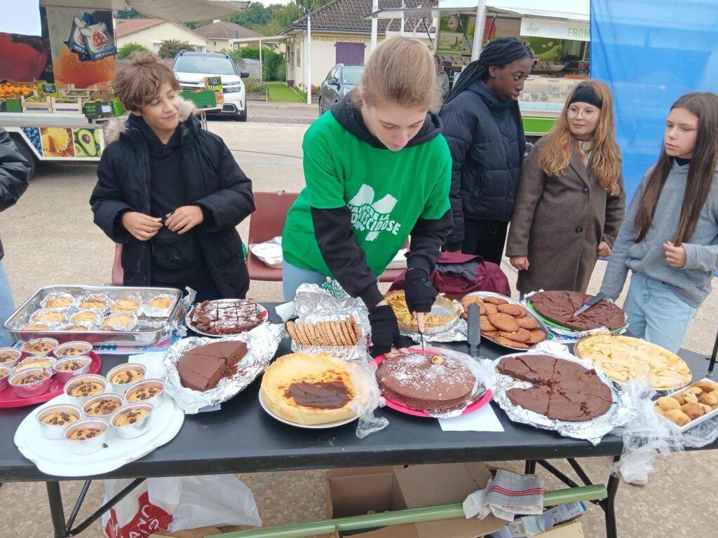 L'image montre un groupe de jeunes gens autour d'une table avec divers desserts, y compris des gâteaux et des tartes, lors d