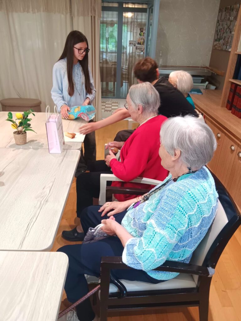 Deux aînées en fauteuils roulants assistées par une jeune femme autour d’une table, activité manuelle en intérieur lum