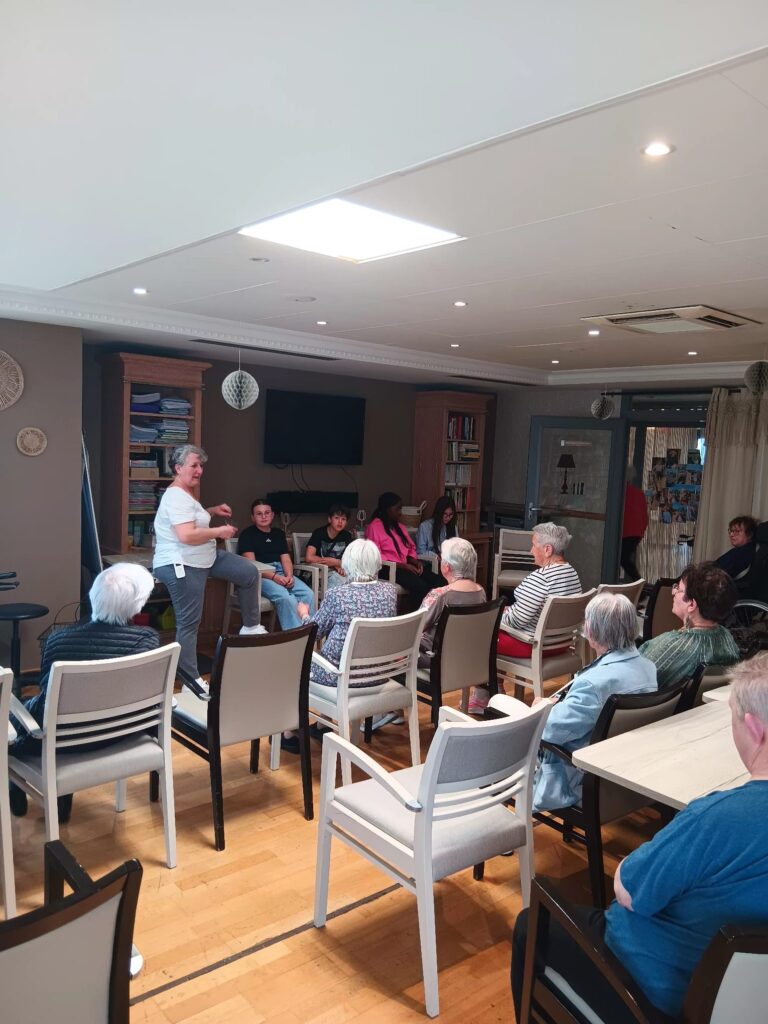 Groupe de personnes assis en cercle écoutant une intervenante dans une salle cosy, ambiance discussion ou atelier.