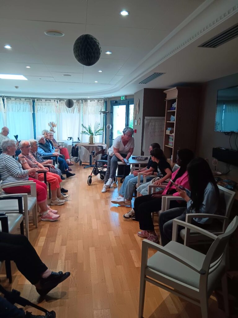 Atelier intergénérationnel : personnes assises en cercle écoutant une animatrice dans une salle lumineuse.