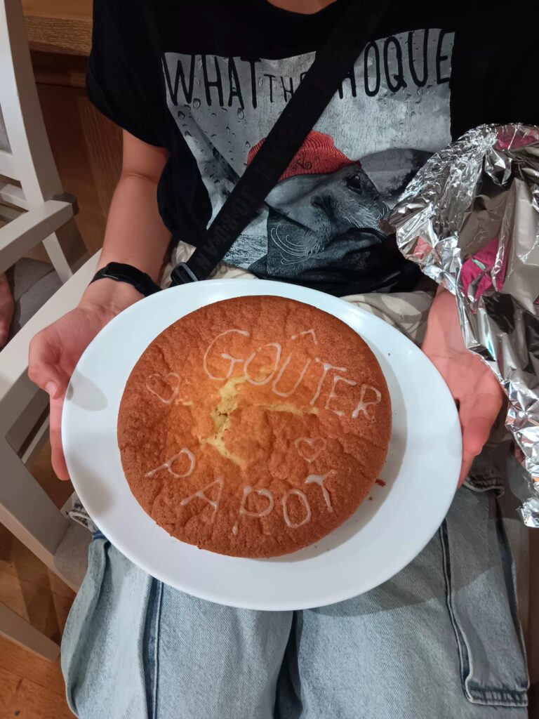 Cake décoré avec écriture "Gouter d'anniv" sur un plat, tenu par une personne en jeans.