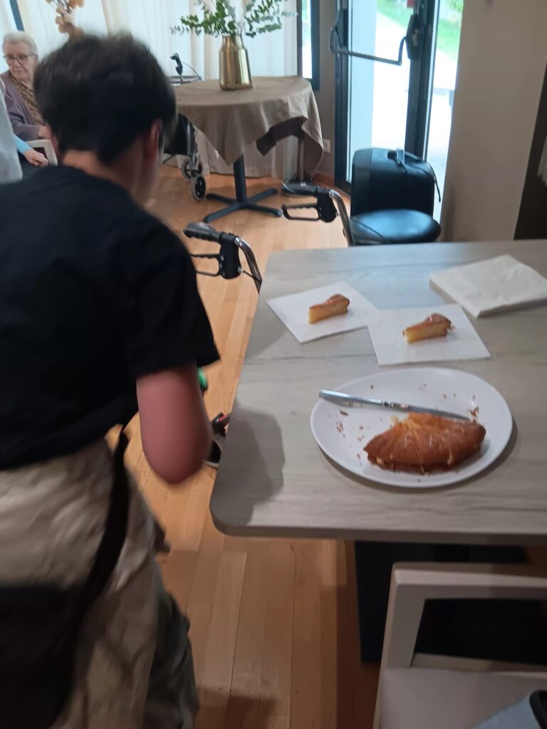 Personnes assises autour d’une table en bois dégustant des pâtisseries, ambiance conviviale et lumineuse.