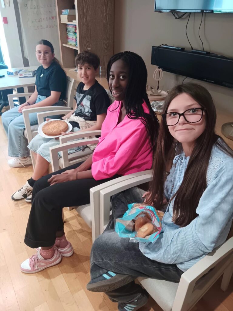 Quatre enfants souriants assis sur des chaises en bois, tenant des bagels, dans une pièce lumineuse.