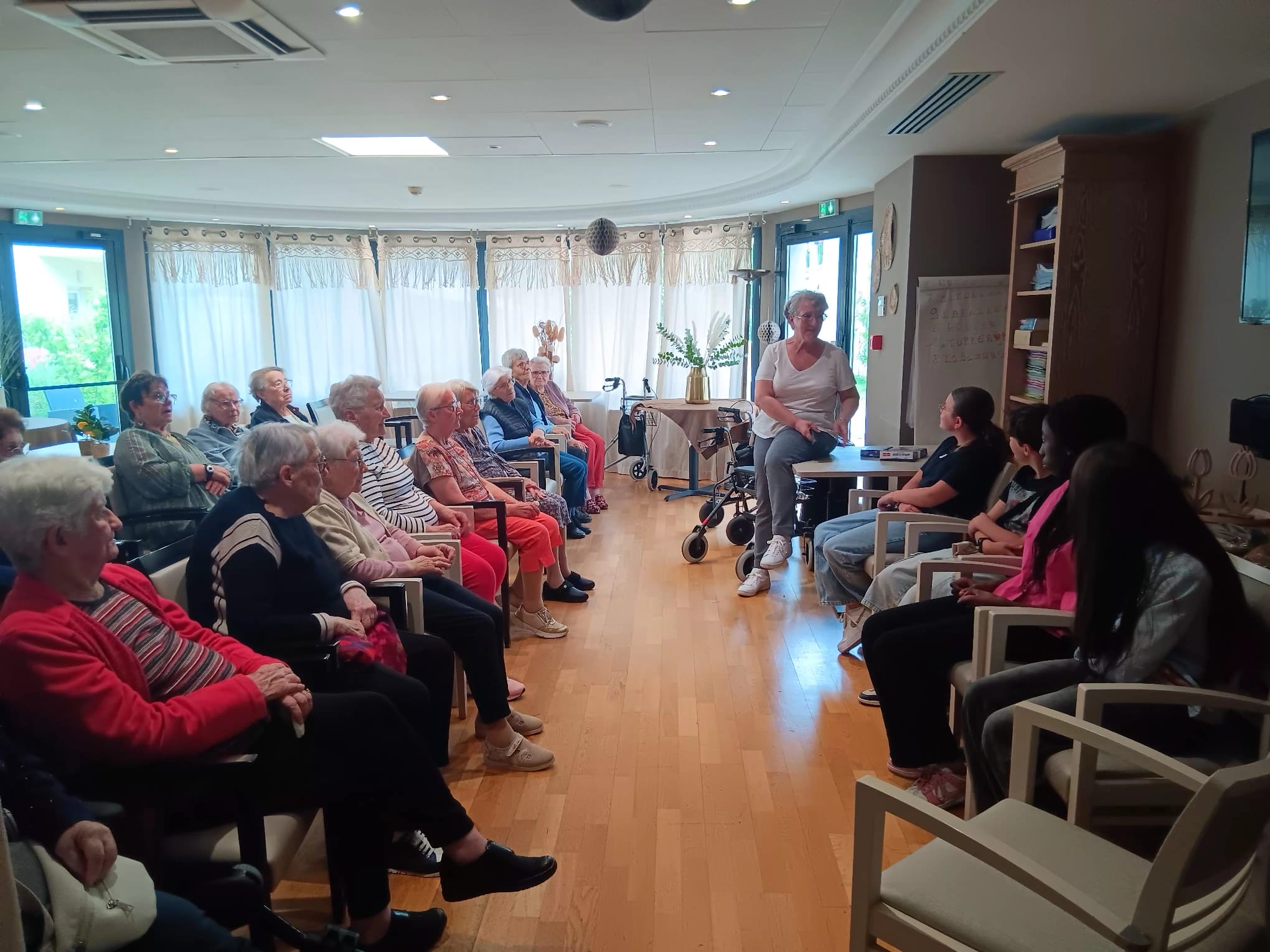 Groupe de seniors assis en cercle écoutant une animatrice dans une salle lumineuse et accueillante.