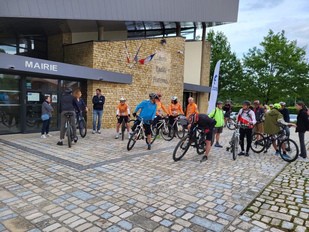Groupe cyclistes devant mairie, équipés, en pause devant bâtiment en briques avec drapeau français.