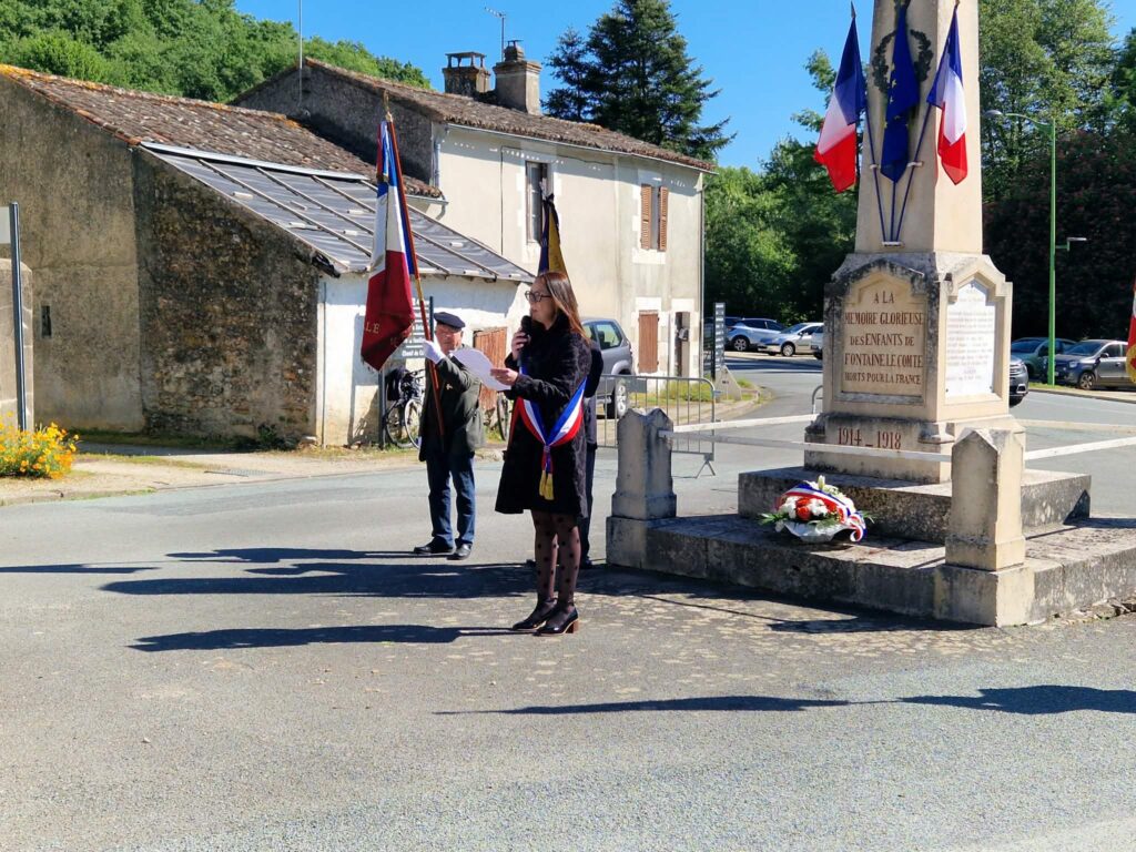Cérémonie commémorative devant un monument aux morts 1914-1918, avec drapeaux français et wreath, en plein jour.