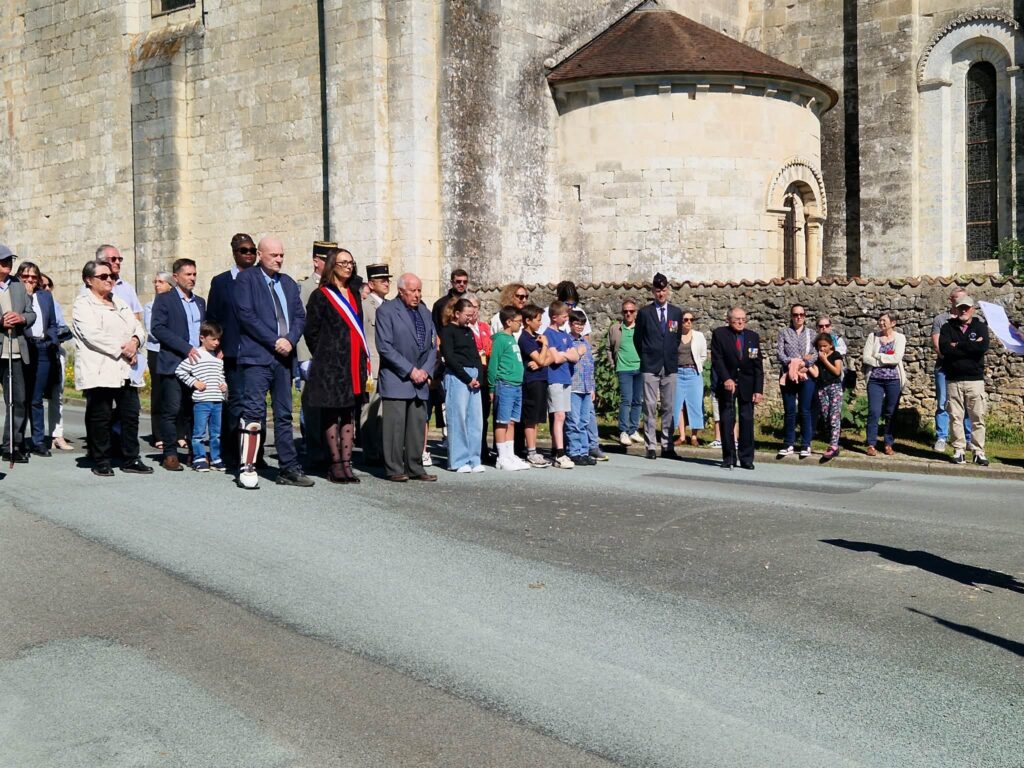 Groupe assemblé devant une vieille église, cérémonie avec drapeaux tricolores et participants variés, enfants et adultes