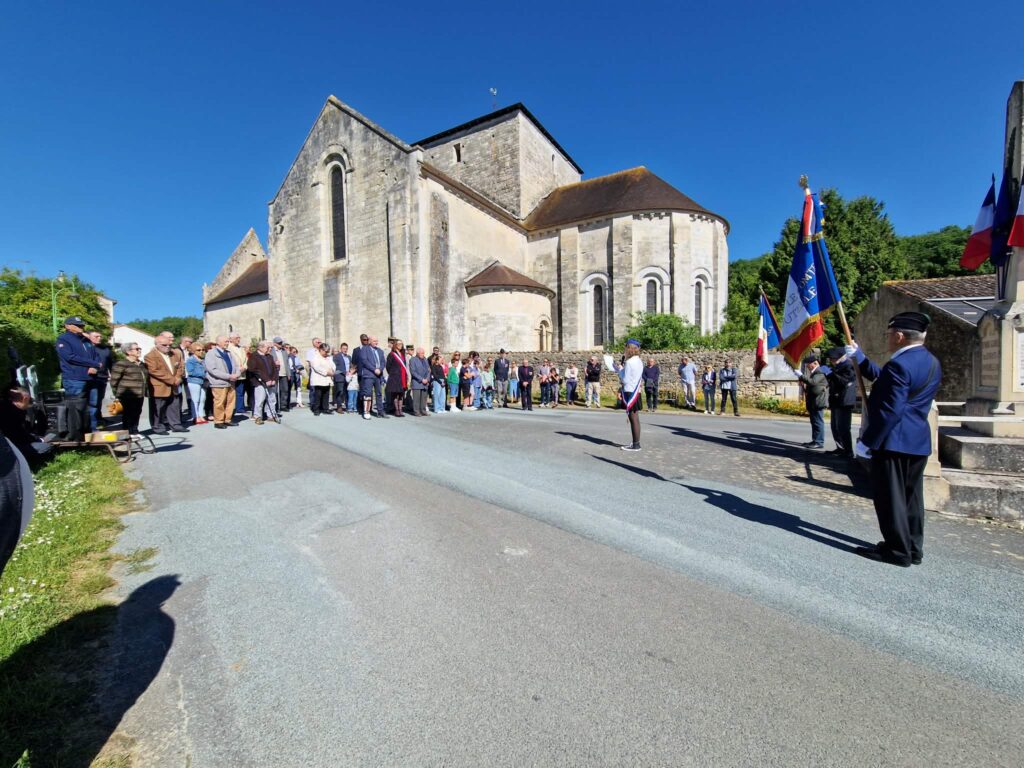 Cérémonie devant une église : groupe assemblé, drapeaux français et locaux, participants en tenue formelle, ambiance com