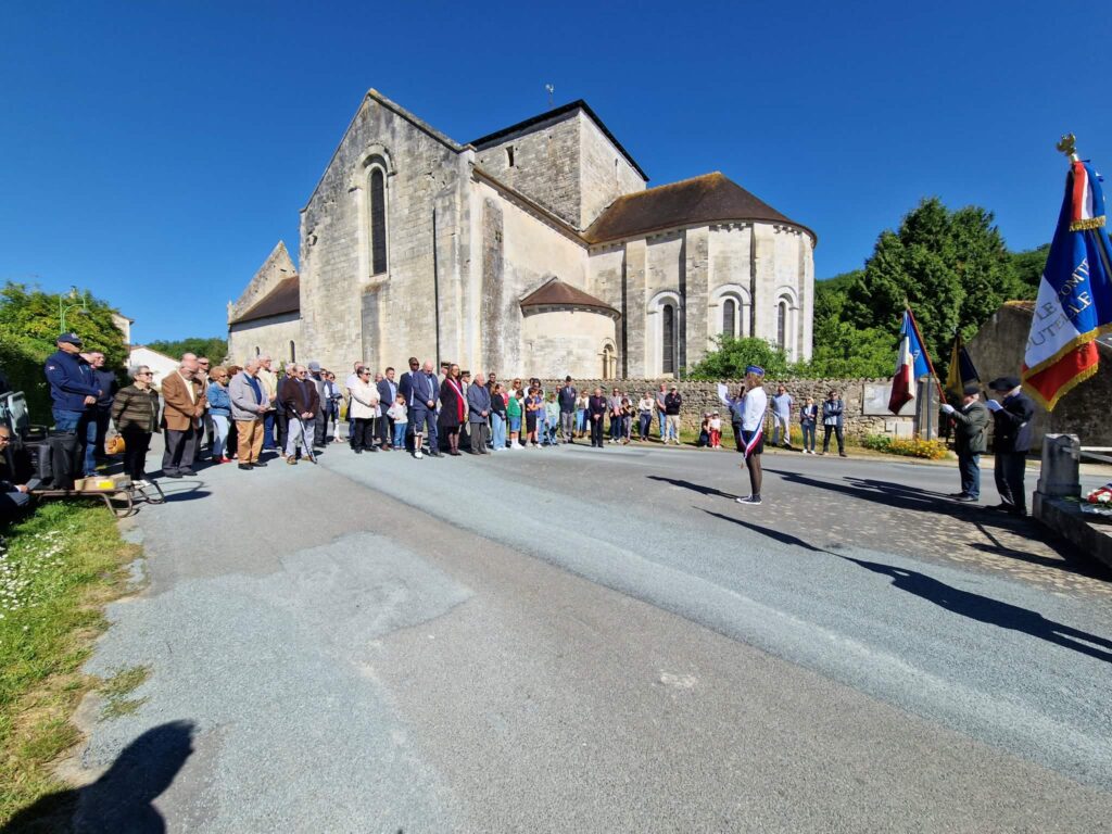 Cérémonie devant une église ancienne : groupe assemblé, drapeaux français, participant en tenue militaire saluant.