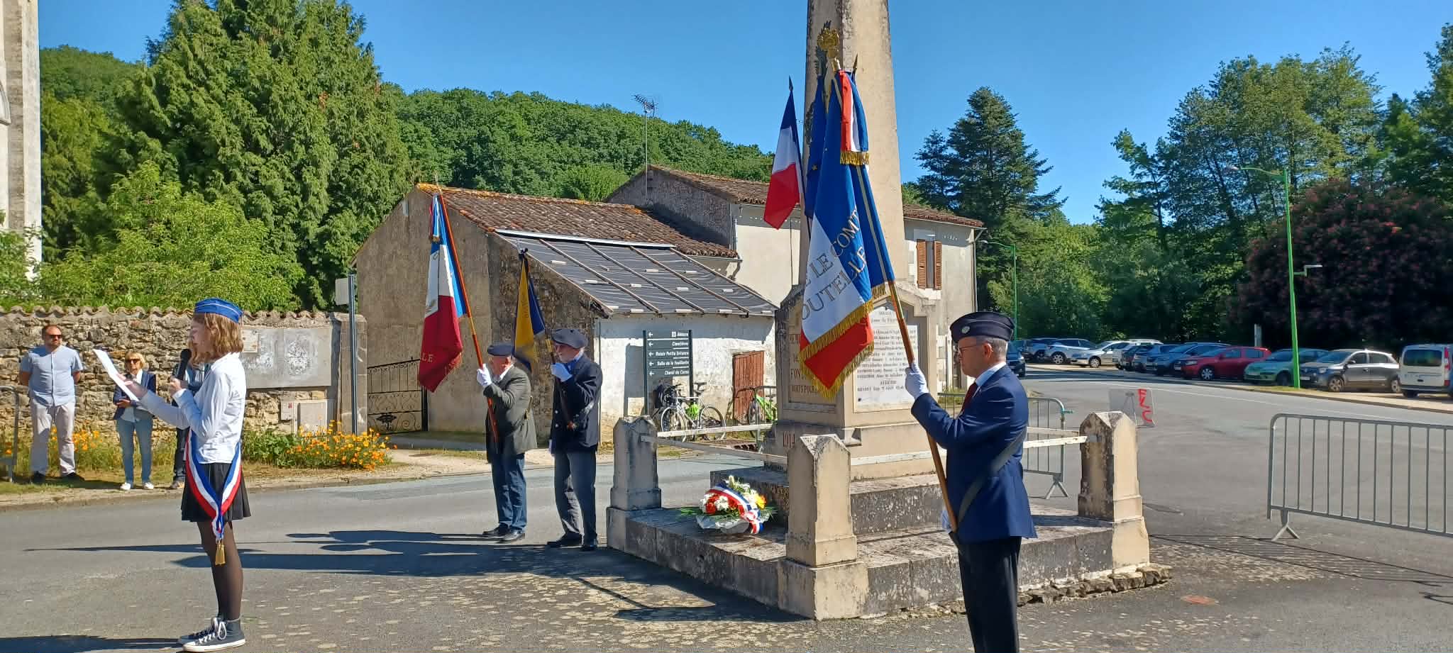 Cérémonie devant monument commémoratif avec drapeaux tricolores et participants en uniforme, sous un ciel dégagé.