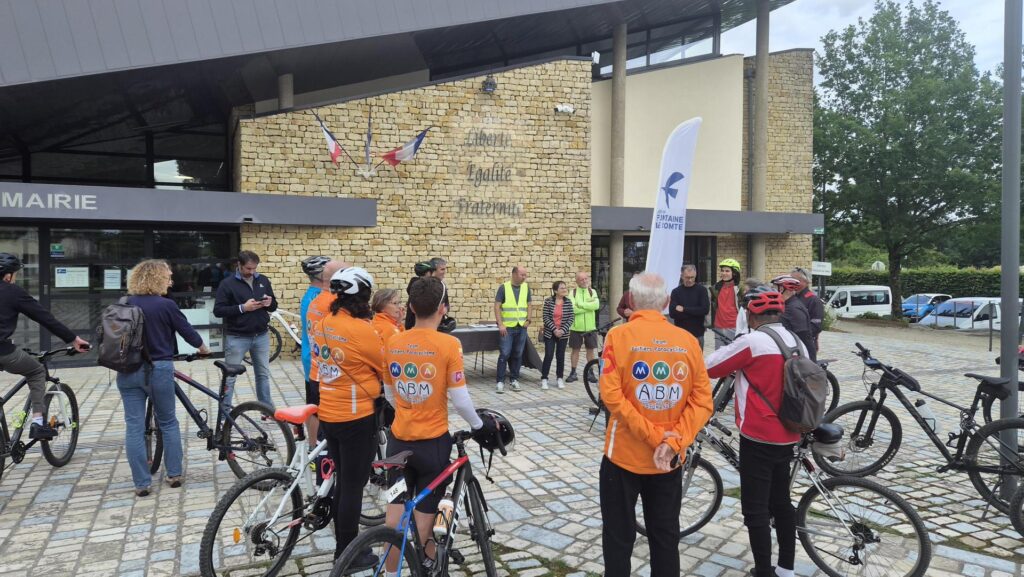 Groupe cyclistes en tenue orange devant mairie, préparation d’une sortie organisée par ABM, sous bannière "Montagne d’