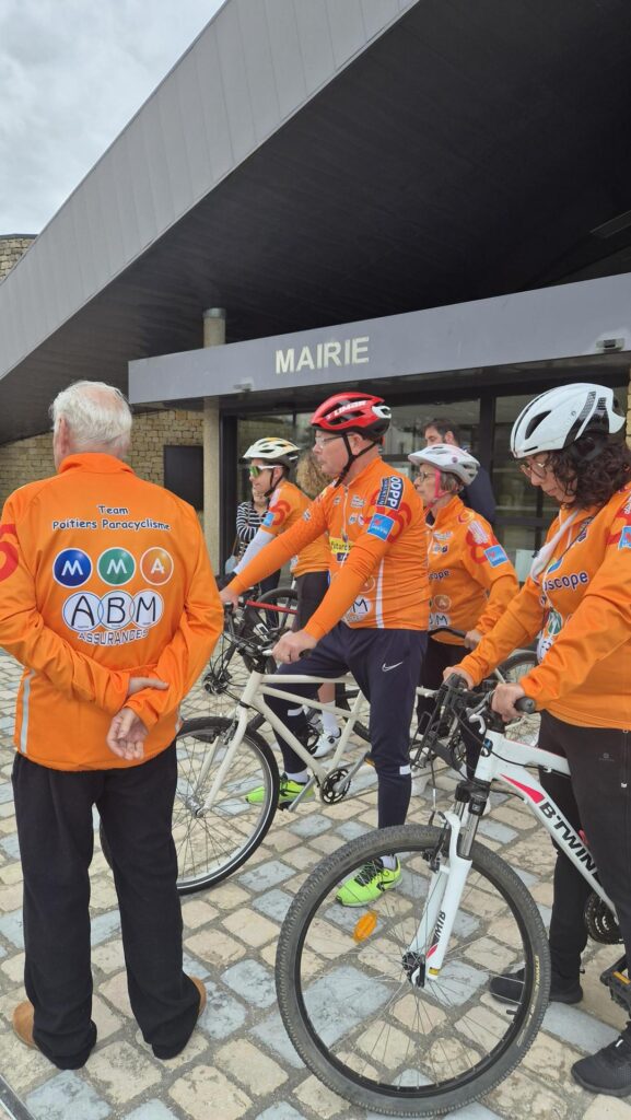 Cyclistes en tenue orange devant une mairie, préparant une sortie avec Team Poitiers Paracyclisme, logos ABM Assurances et M