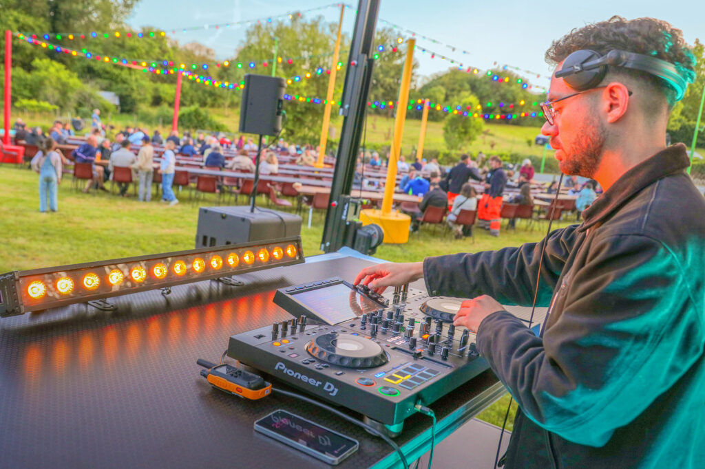 DJ manipulant une table de mixage Pioneer à l’extérieur lors d’un événement festif avec public en fond.