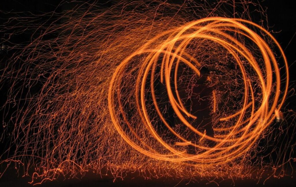 Traînées lumineuses orange formant des spirales sur fond noir, effet de lumière dynamique.