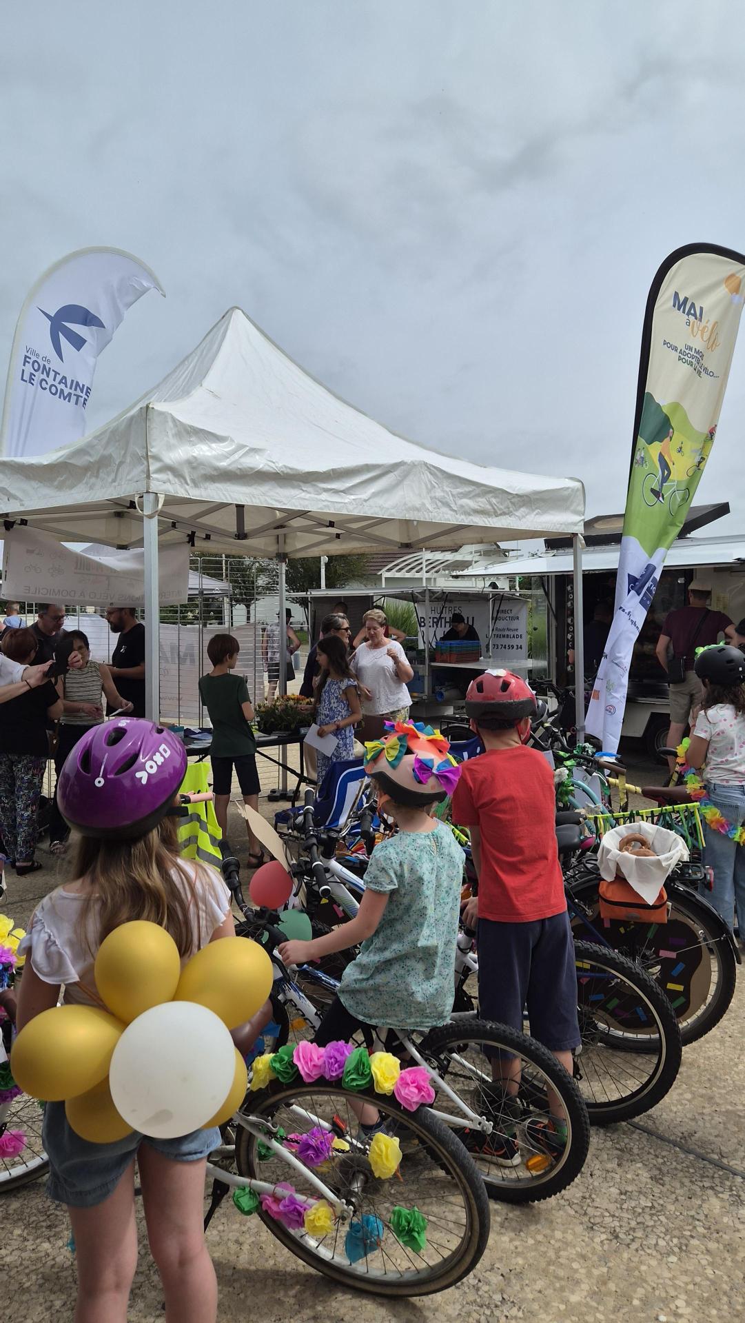 Enfants en fête avec casques et vélos décorés, ballons, sous tente événementielle "Ville de Fontaine-le-Comte".