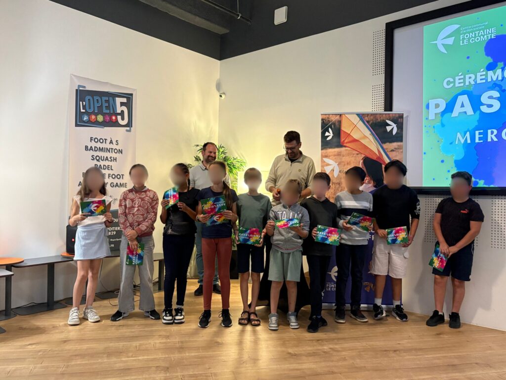 Cérémonie remise de prix "Pass Loisirs" : enfants souriants recevant des cadeaux, encadrés par des adultes, dans un centre