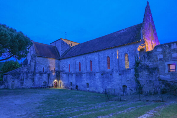 Ancienne abbaye illuminée au crépuscule, vue de nuit avec clocher et façade en pierre.