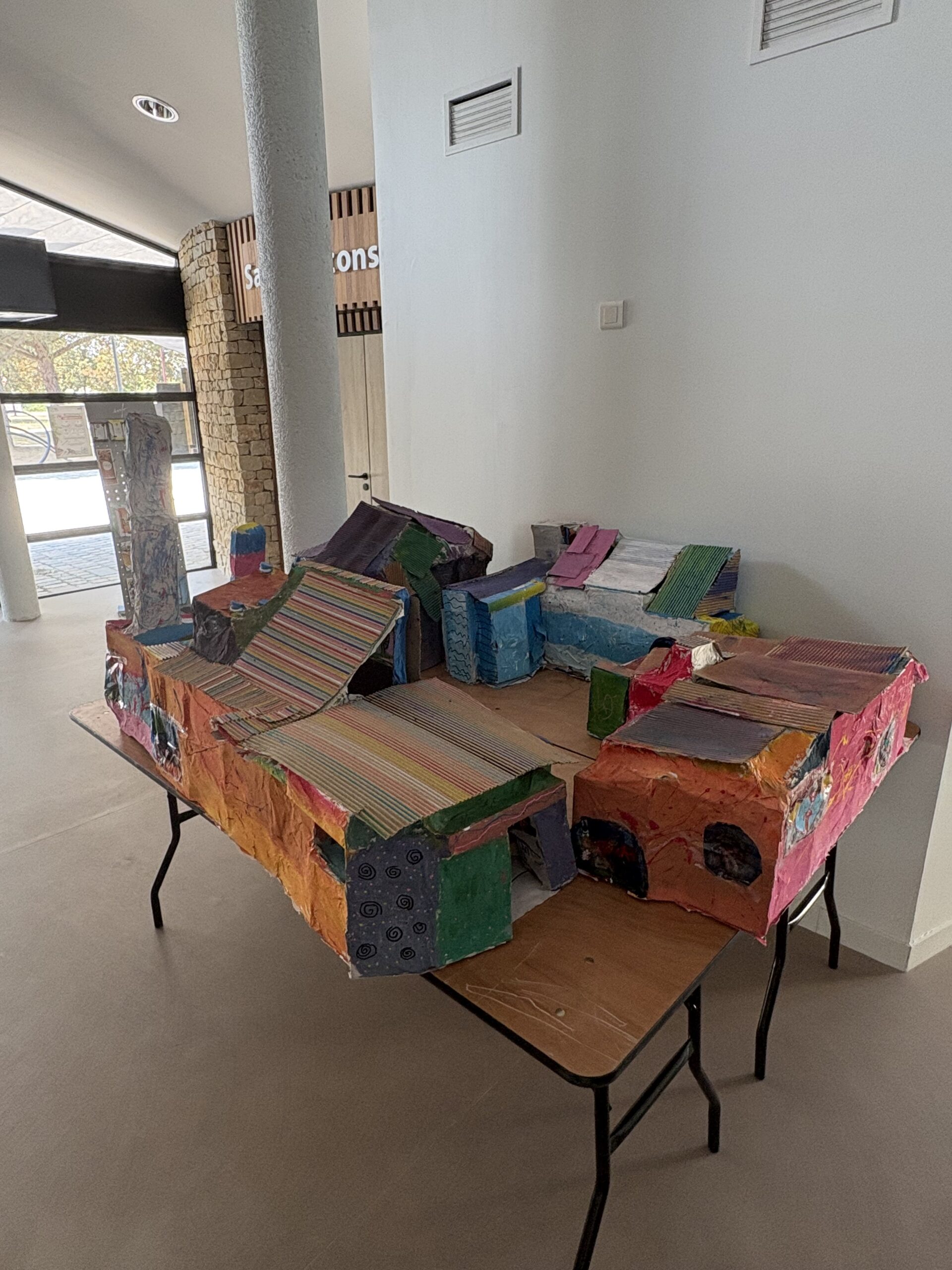 Table décorée avec des coussins colorés et motifs variés, exposée dans une pièce lumineuse. Artisanat créatif.
