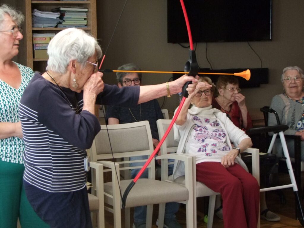 Personnes âgées participant à un exercice avec des bâtons colorés, assises sur des chaises dans une salle.