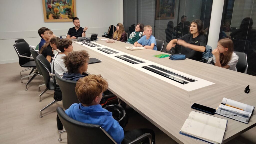 Groupe d’enfants et adultes en réunion autour d’une table, discutant dans une salle moderne.