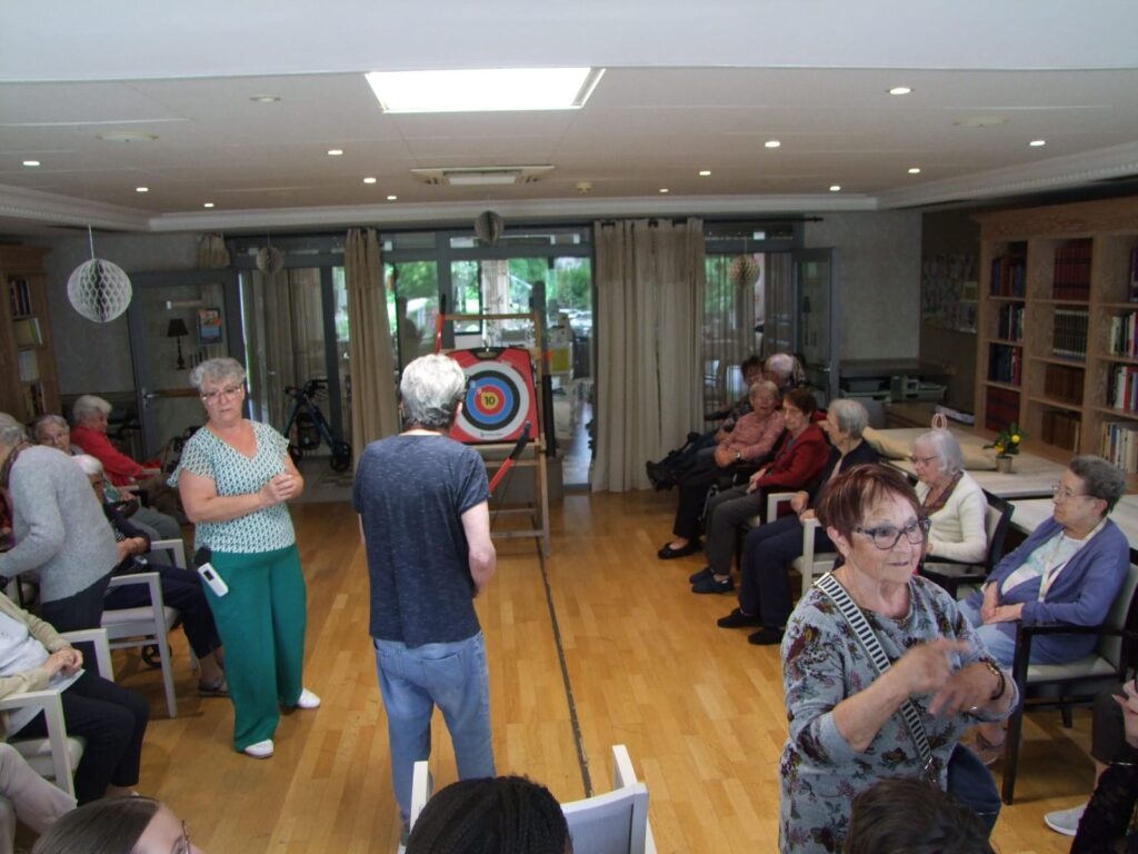 Groupe d’adultes participant à un atelier d’archerie en intérieur, observant et discutant.