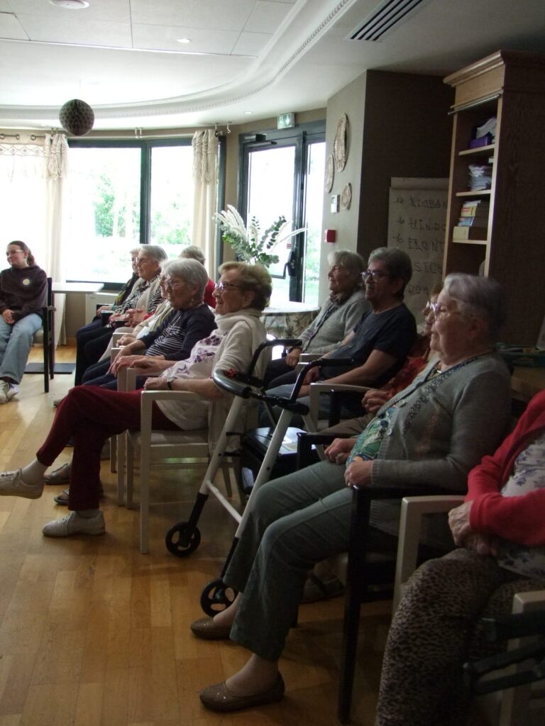 Groupe de personnes âgées assis en cercle dans une salle lumineuse, participant à une réunion ou activité sociale.