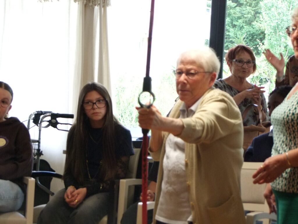 Un homme montre une montre à l’assistance, public assis en discussion, lumière naturelle. Événement éducatif ou démon