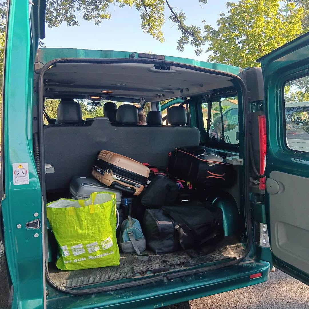 Cabine de van verte remplie de bagages et sacs, dont un sac jaune et des valises, prête pour un voyage.