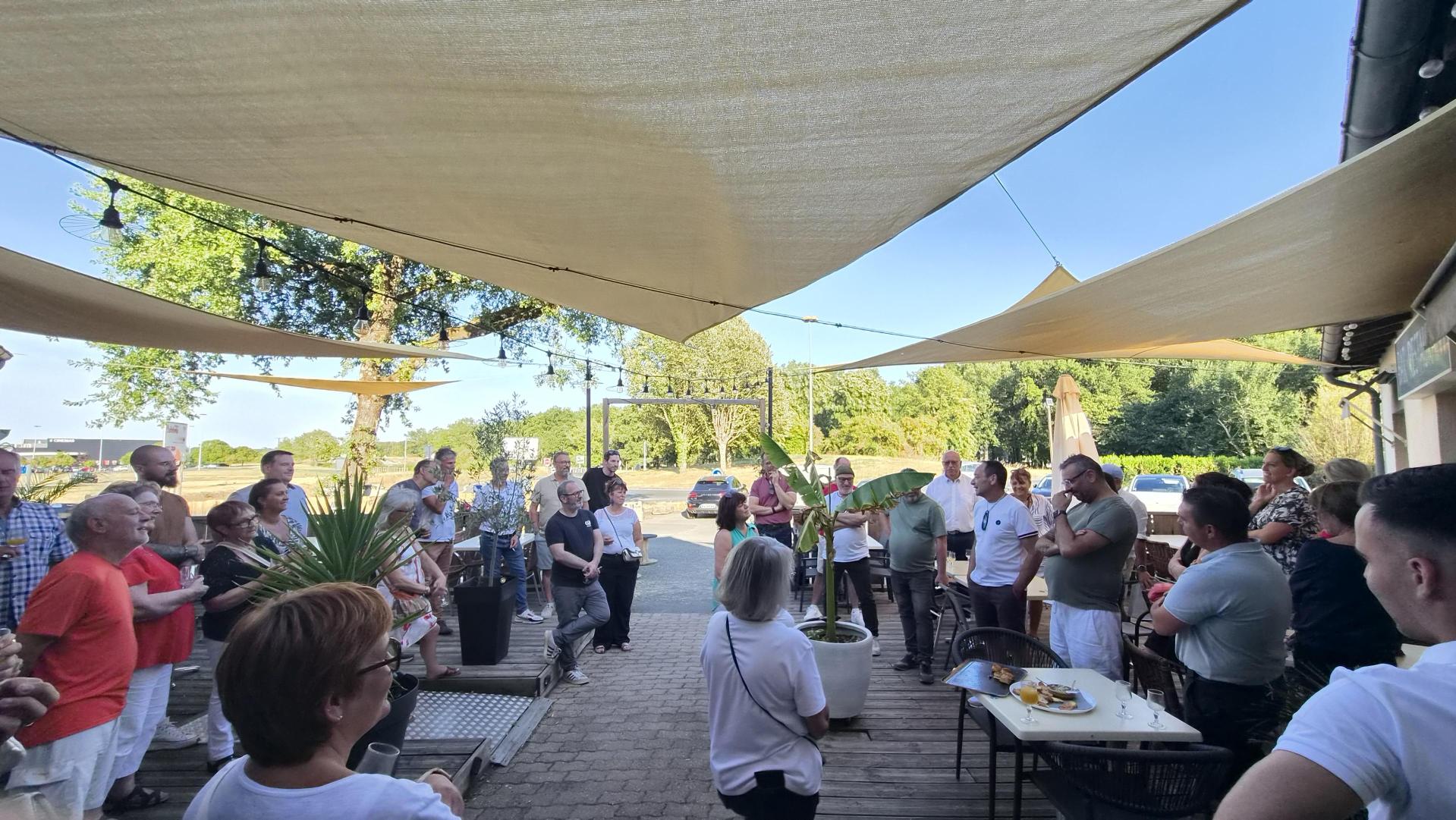 Groupe de personnes réunies sous une pergola en extérieur, discutant et mangeant en plein air, ambiance conviviale et ensol