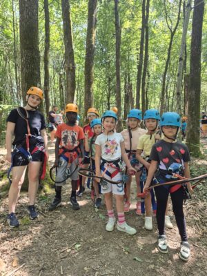 Un groupe d’enfants et un adulte équipés de casques et harnais, prêts pour une activité d’accrobranche en forêt.