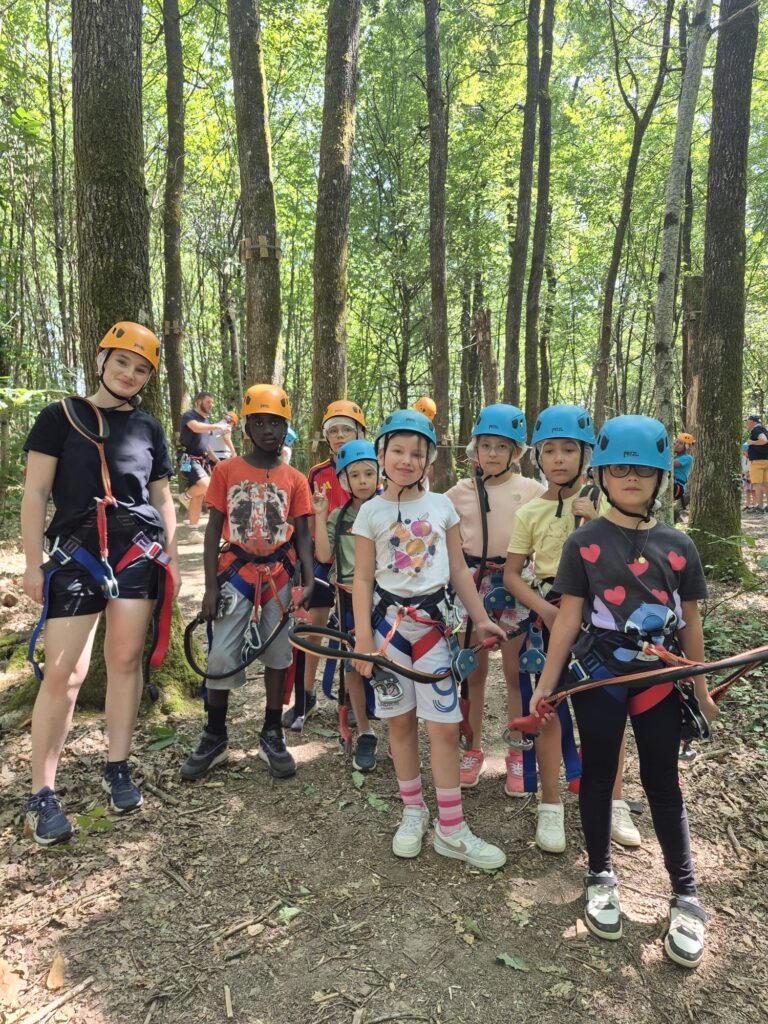 Un groupe d’enfants et un adulte équipés de casques et harnais, prêts pour une activité d’accrobranche en forêt.