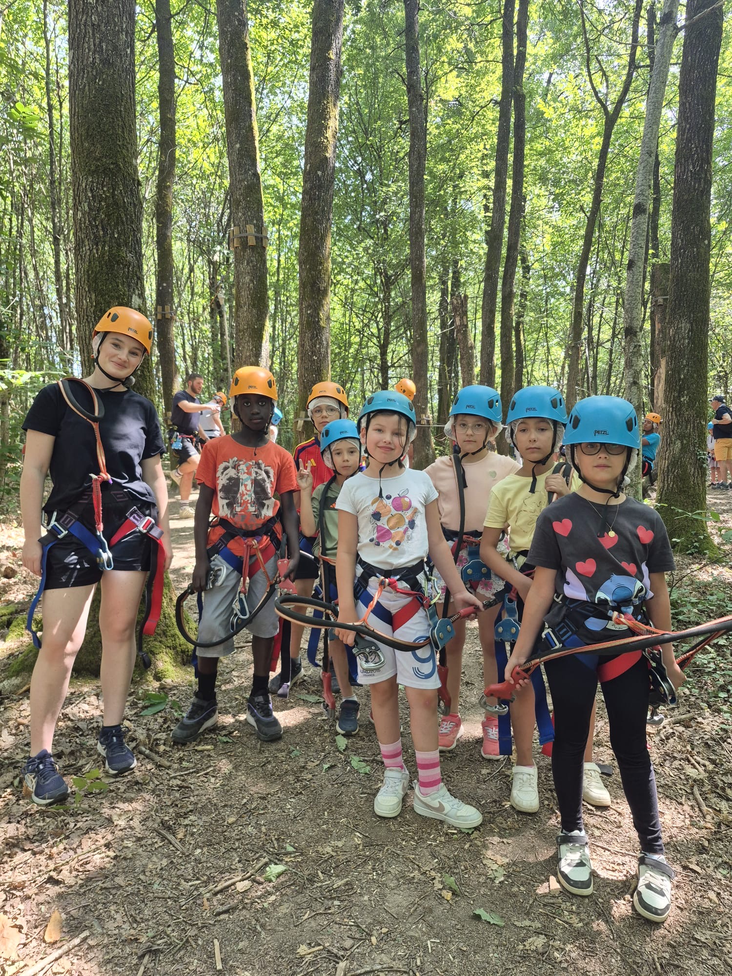 Un groupe d’enfants et un adulte équipés de casques et harnais, prêts pour une activité d’accrobranche en forêt.