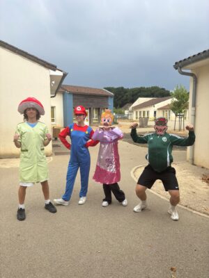 Quatre personnes déguisées en personnages de Mario, poses dynamiques devant un bâtiment scolaire.