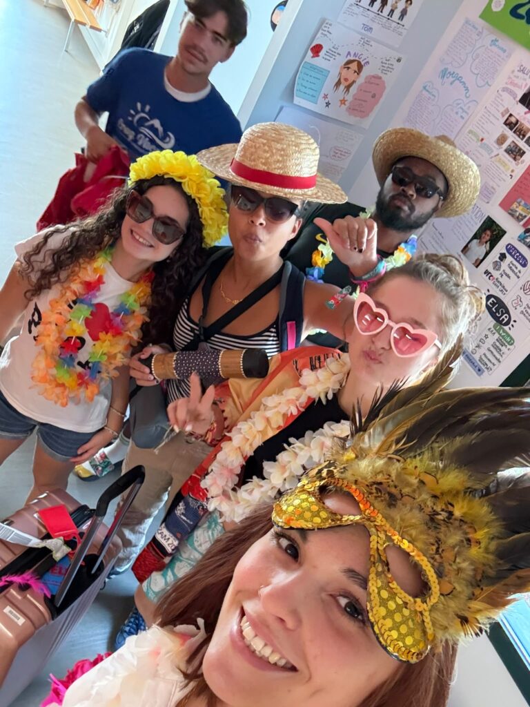 Groupe joyeux en tenues festives hawaïennes, posant souriants devant un panneau coloré.