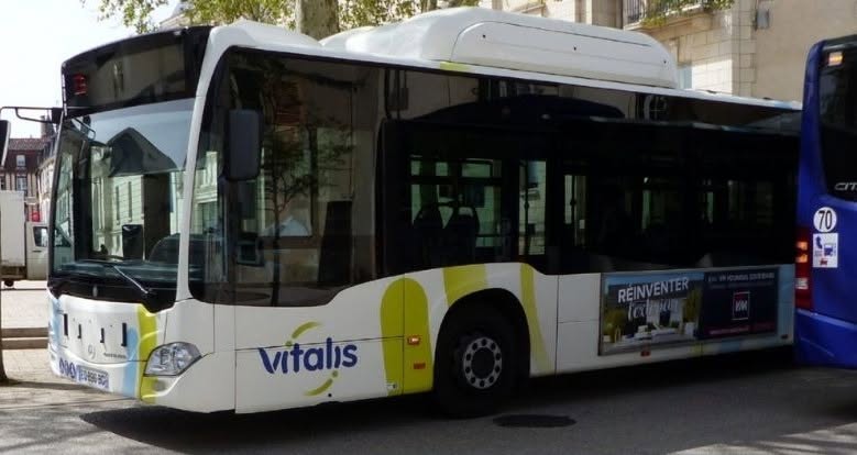 Bus Vitalis blanc et jaune, stationné en ville, affichant une pub pour "Reinventer la cuisine".