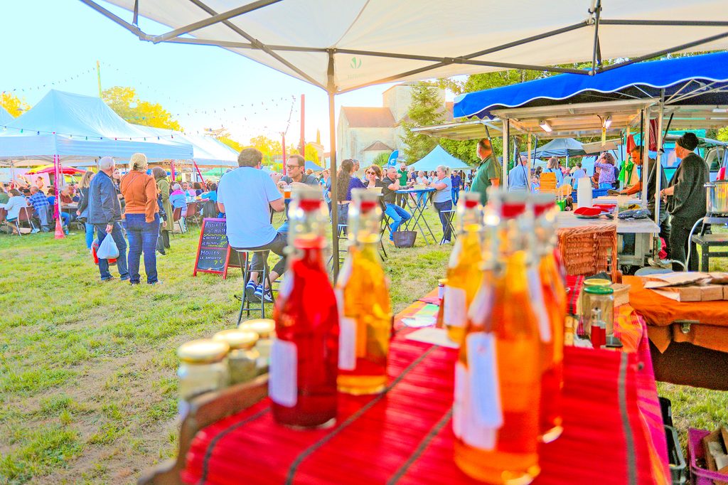 Marché artisanal en plein air avec étals colorés et visiteurs sous tentes, ambiance conviviale et produits locaux.