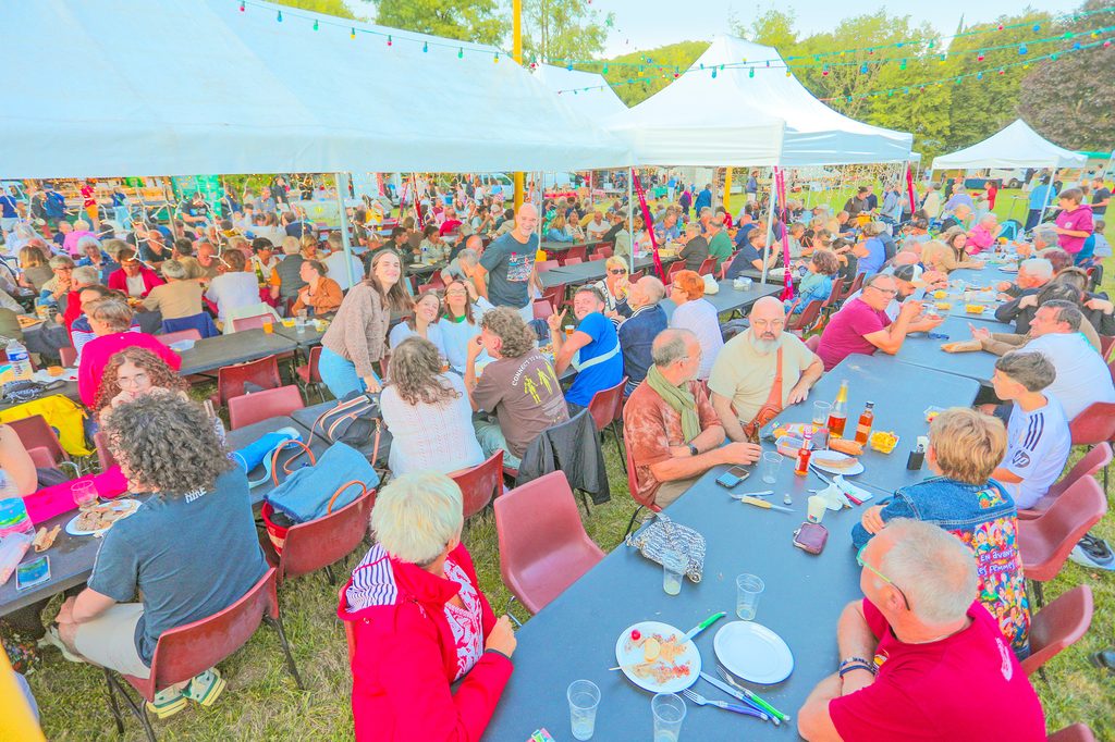 Groupe convivial sous tentes colorées lors d’un repas en plein air, ambiance festive et animée.