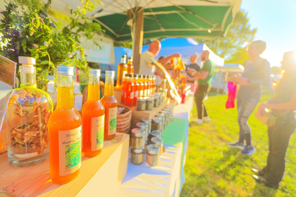 Bouteilles de sirop et condiments exposés sur un comptoir ensoleillé, ambiance festive en extérieur avec plantes et paraso