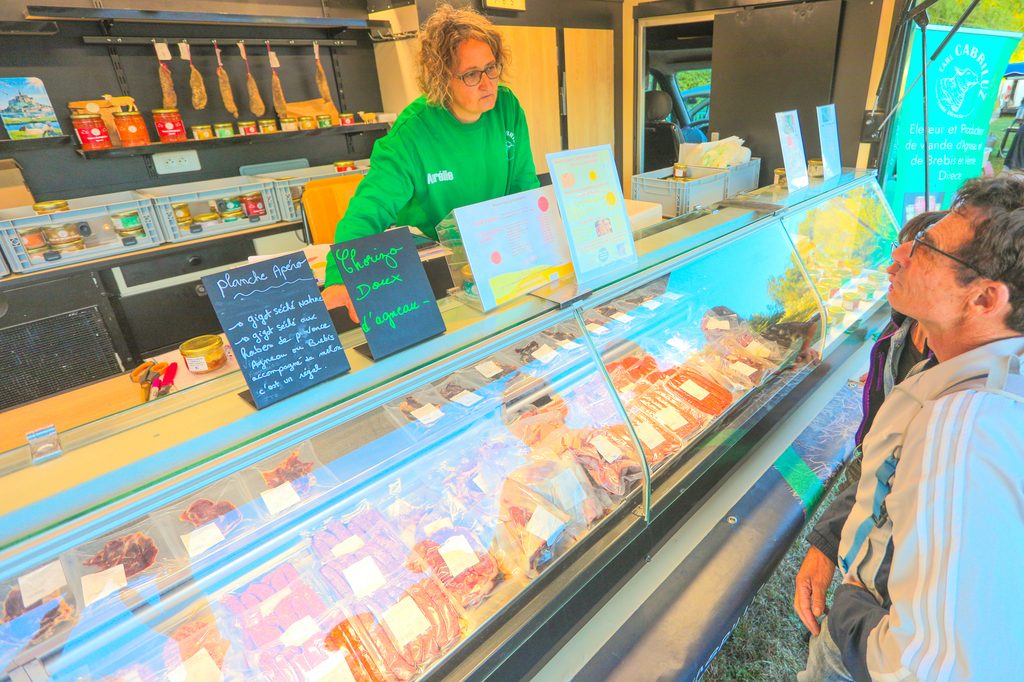 Une employée en vert discute avec un client devant un comptoir de produits frais et poissons sous vitrine.