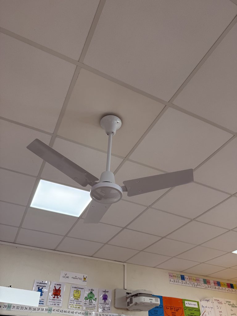 Ce plafond suspendu montre un ventilateur et un éclairage dans une salle de classe avec affiches éducatives.