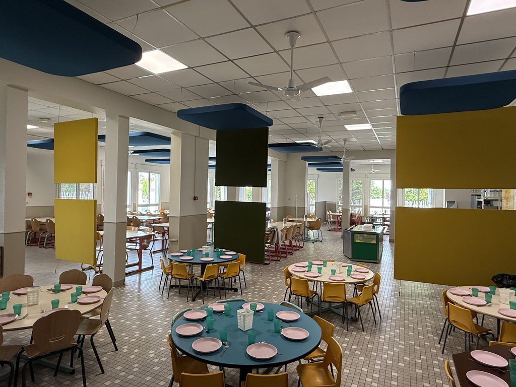 Cafétéria spacieuse avec tables rondes, chaises et sets de table, éclairage moderne et colonnes colorées.