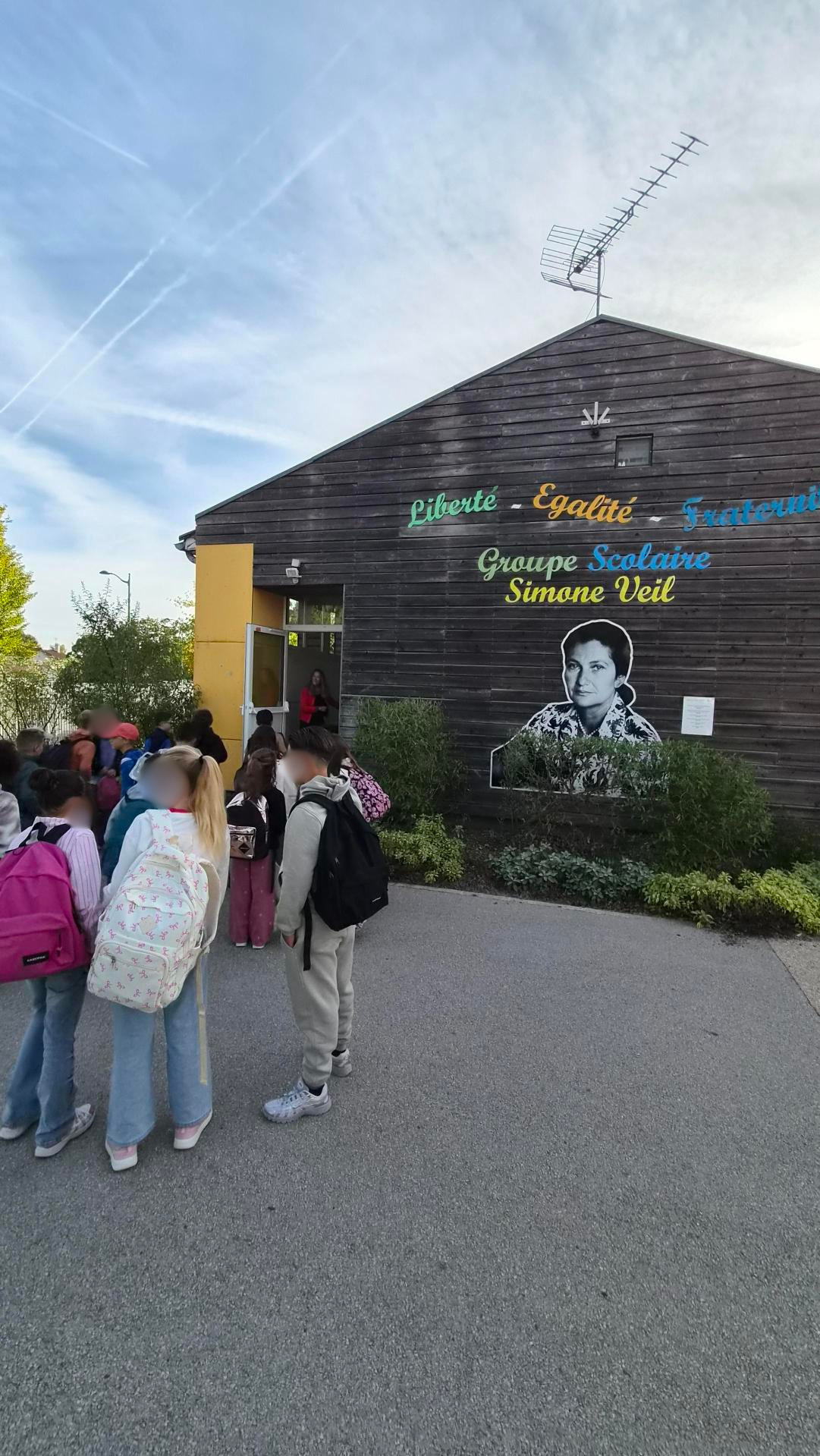 École "Groupe Scolaire Simone Veil" : enfants devant bâtiment avec portrait, slogans "Liberté-Égalité-Fraternité".