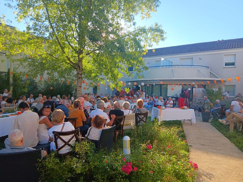 Groupe d’aînés assis en extérieur lors d’un événement festif sous tentes et décorations colorées.