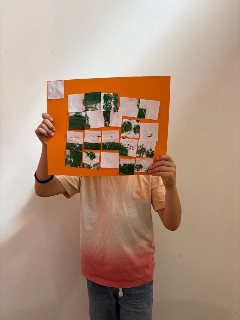 Une personne tient une affiche orange avec des carrés verts et blancs représentant des paysages, masquant son visage.