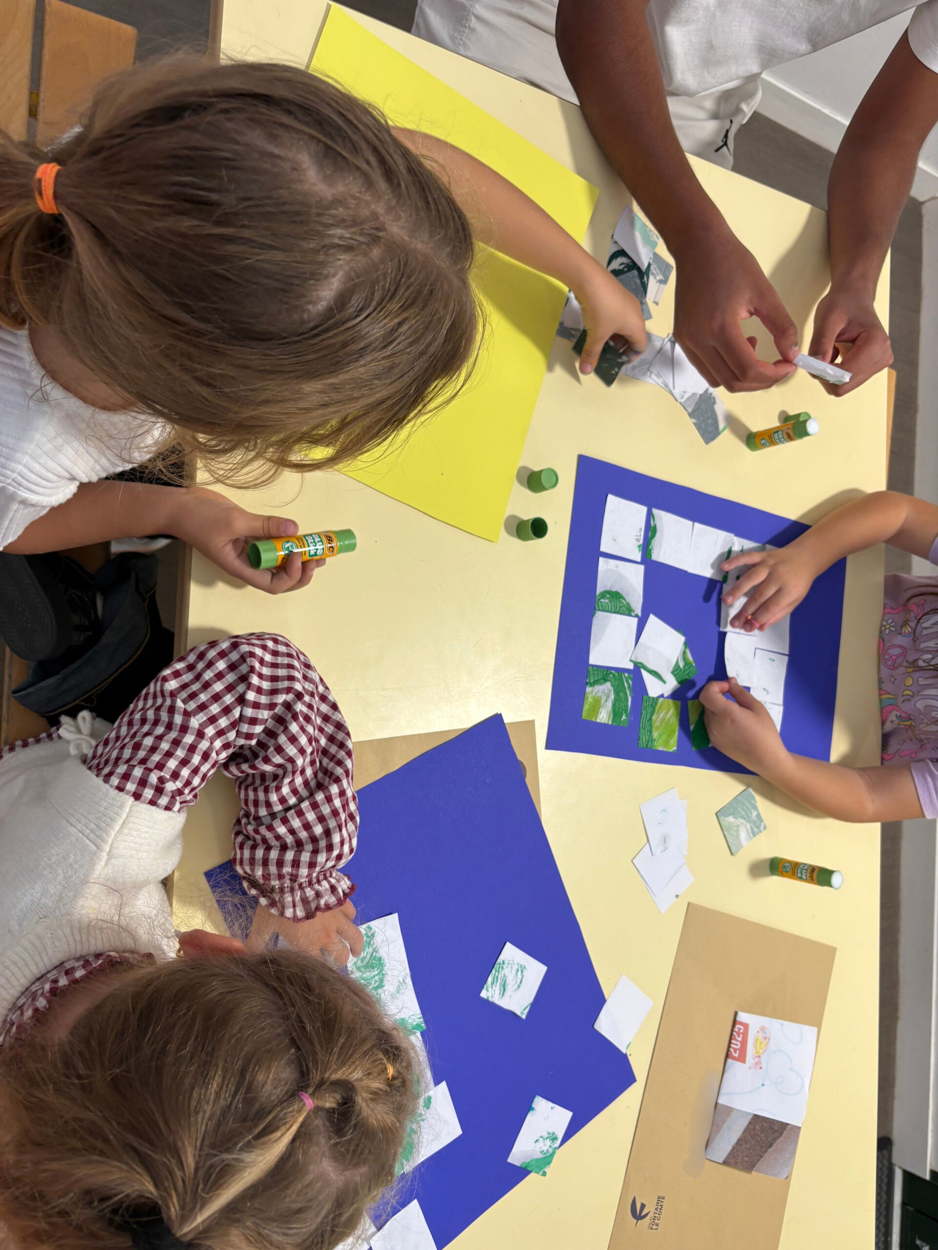 Enfants collant et dessinant avec des crayons verts sur des feuilles colorées, activité créative en groupe.