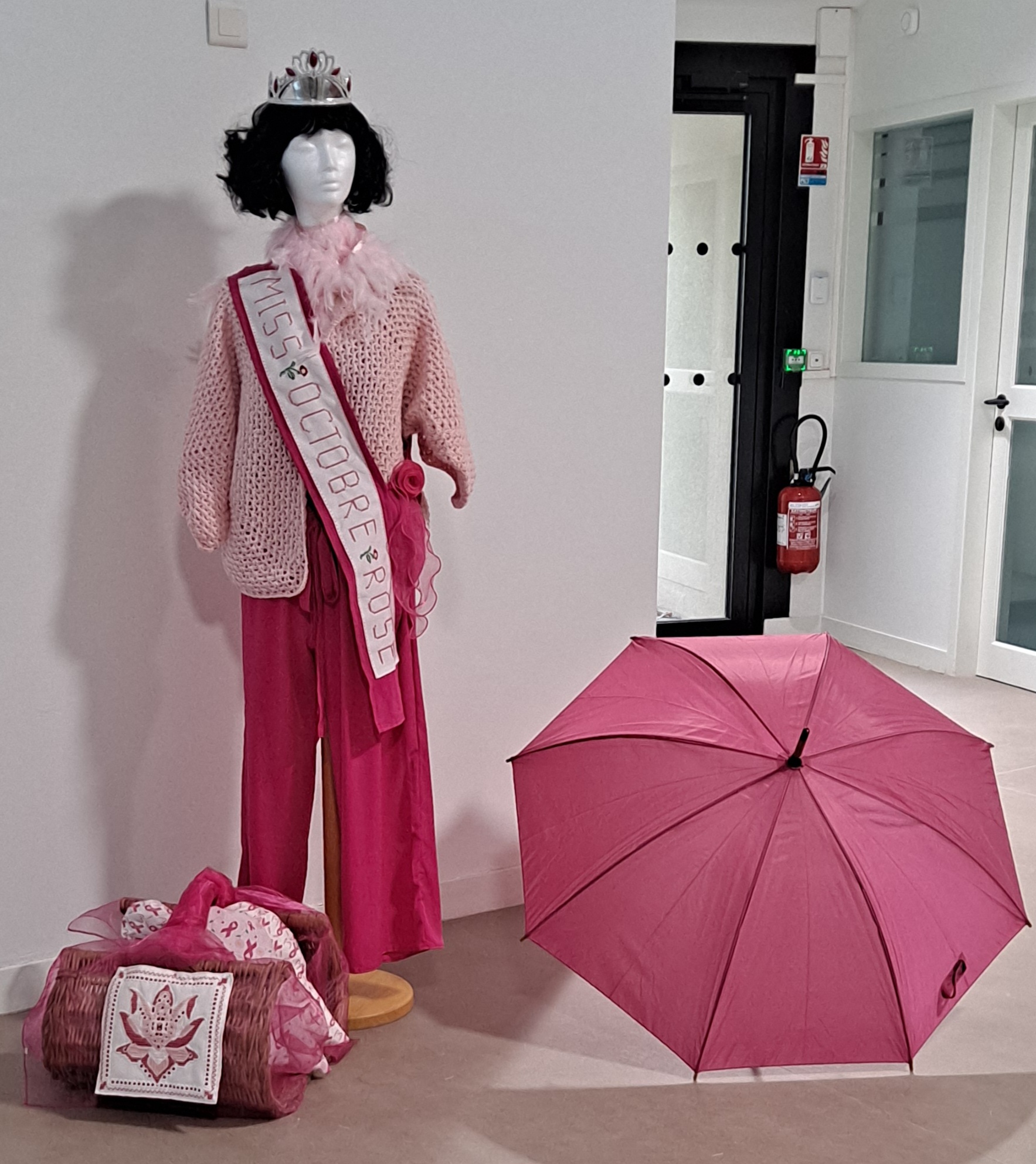 Mannequin vêtu d’une robe rose avec sash "Miss Octobre Brest", couronne, écharpe et parapluie rose, accessoires posés au