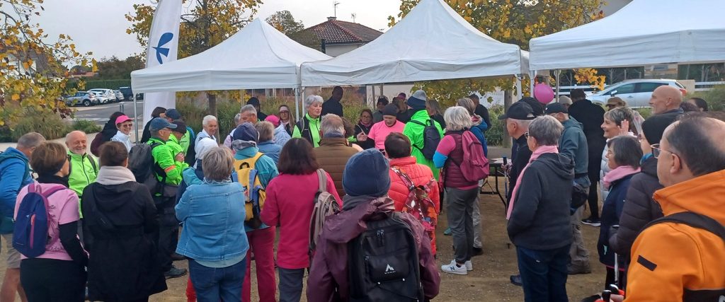 Groupe de personnes réunies sous une tente lors d'un événement extérieur, discutant et portant des vestes colorées.